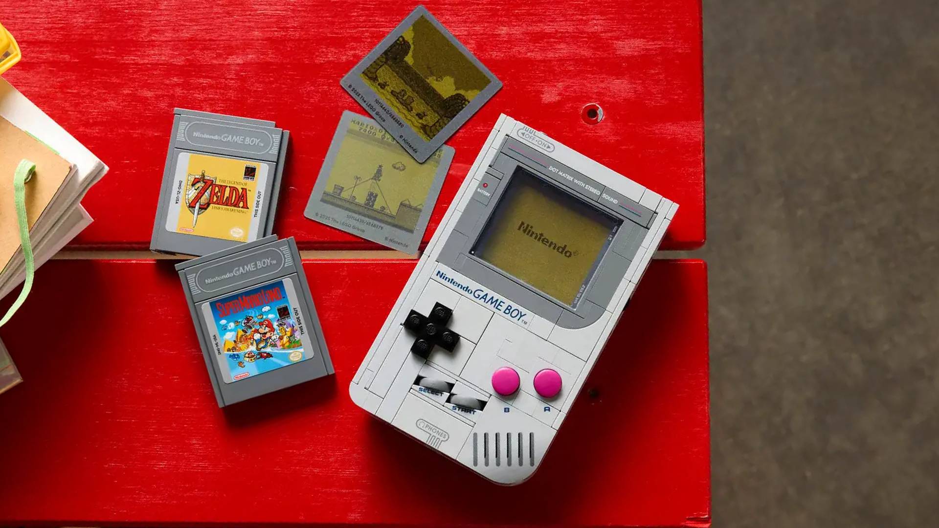 Lego Game Boy kit on red table next to Zelda and Mario cartridges and matching lenticular inserts.