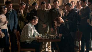 Two characters playing an intense game of chess surrounded by a large group of people
