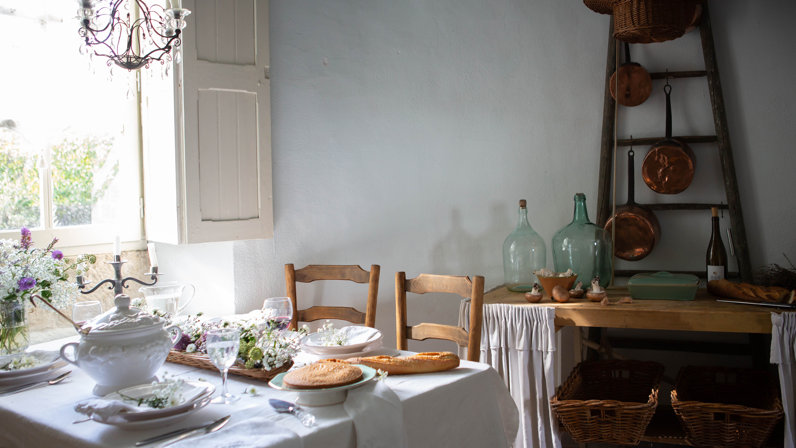 view of dining table beside window with shutters in french tower with rustic ladder and copper pans behind