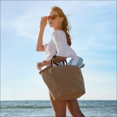 Woman carrying straw beach bag with towel in front of the ocean