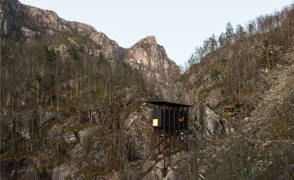 View of Peter Zumthor’s zinc mining museum - a black structure with a wooden frame that sits in the middle of rocky cliff sides