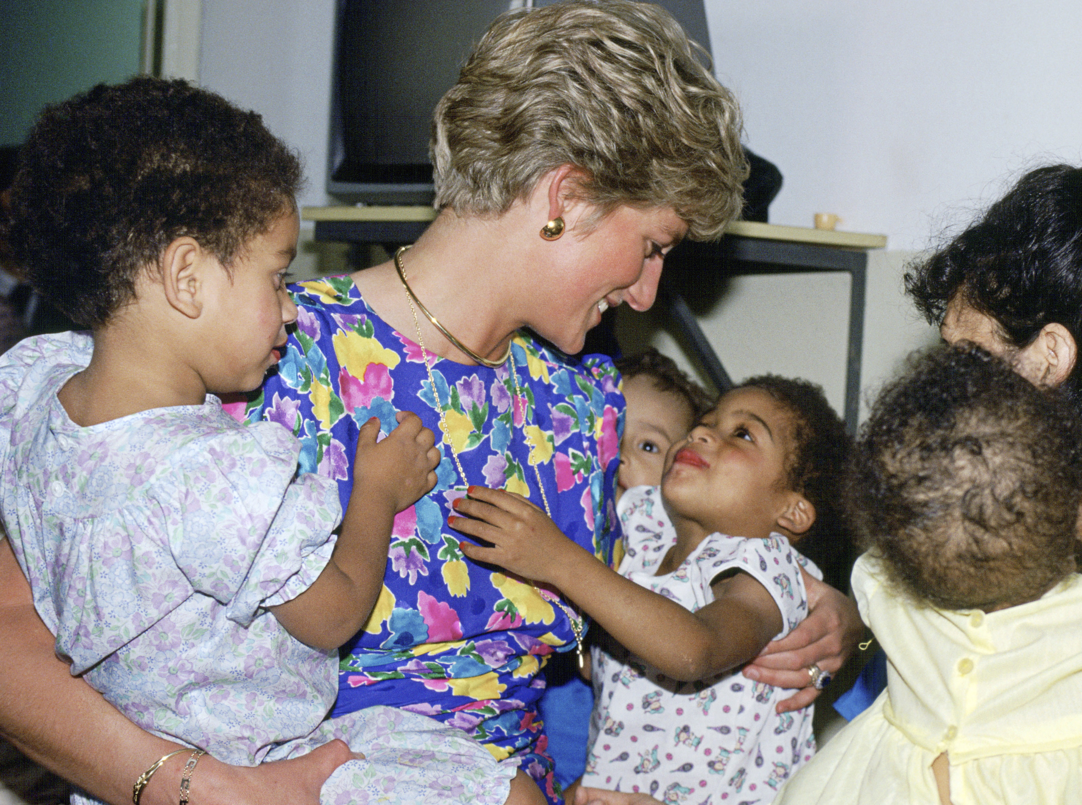 Princess Diana wearing a blue floral dress holding two children