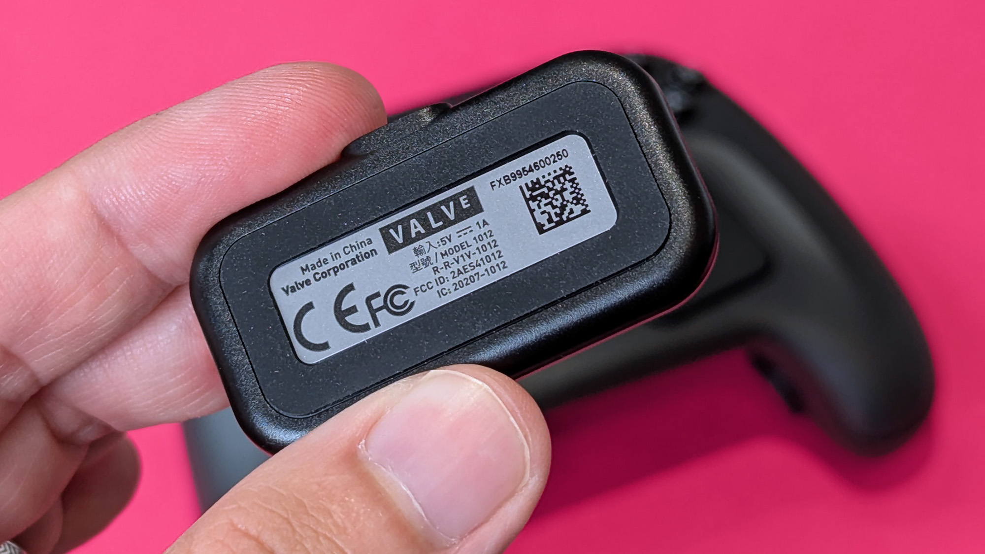 Charging puck information on the Valve Steam Controller (2026) held in hand against a magenta card background