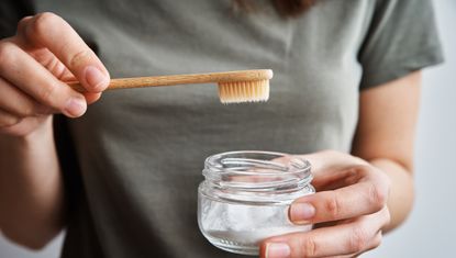 woman holding toothbrush near lid of powdery substance