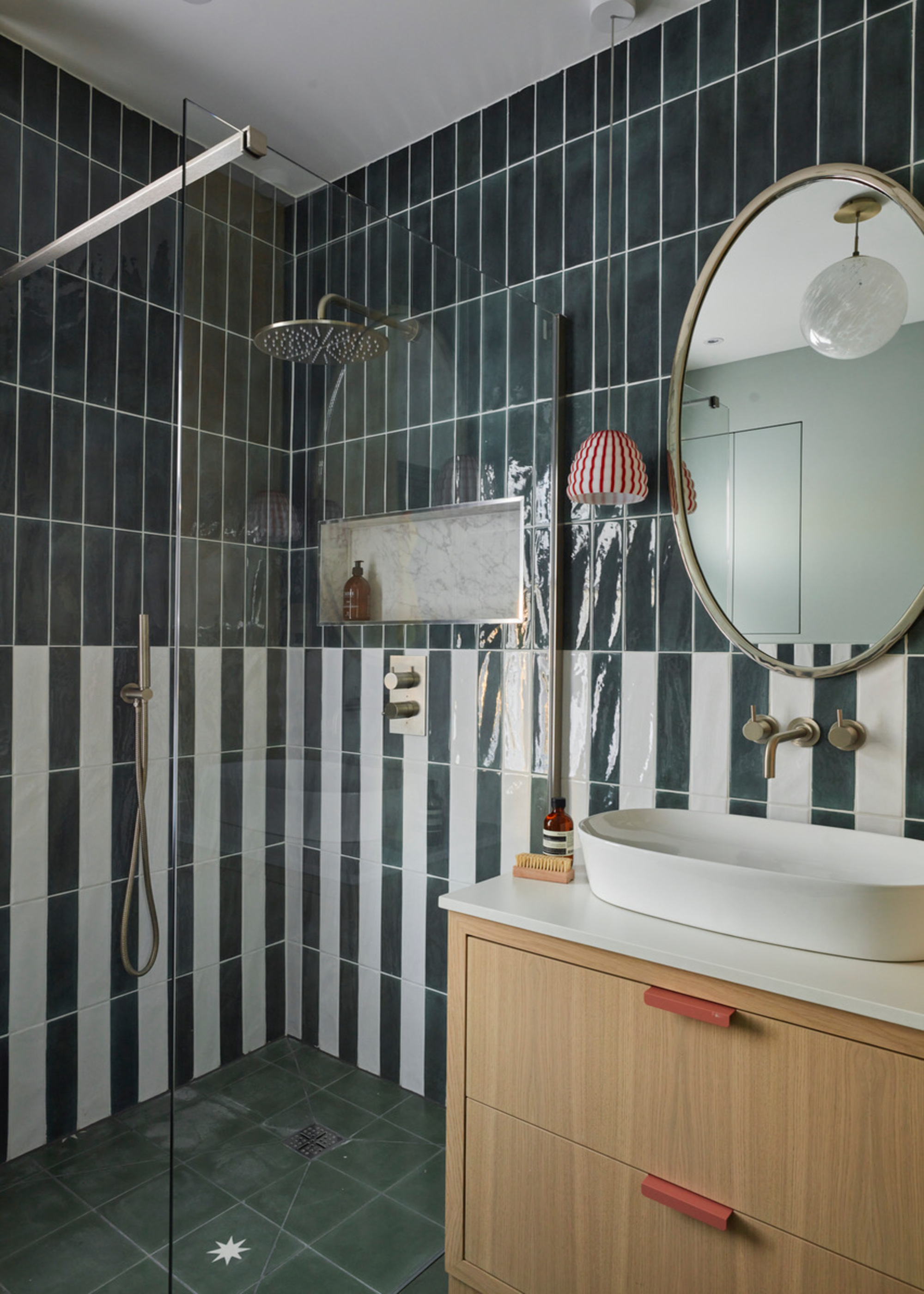 A bathroom with green and white striped tiles and a modern vanity with red drawer pulls