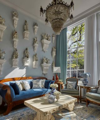 A light blue sitting room with an antique console, a blue velvet couch, and ornate decorative accessories in porcelain and gold