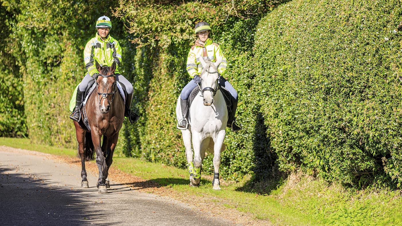 Two riders hack down a country lane wearing high vis. Confidence horse riding on the road