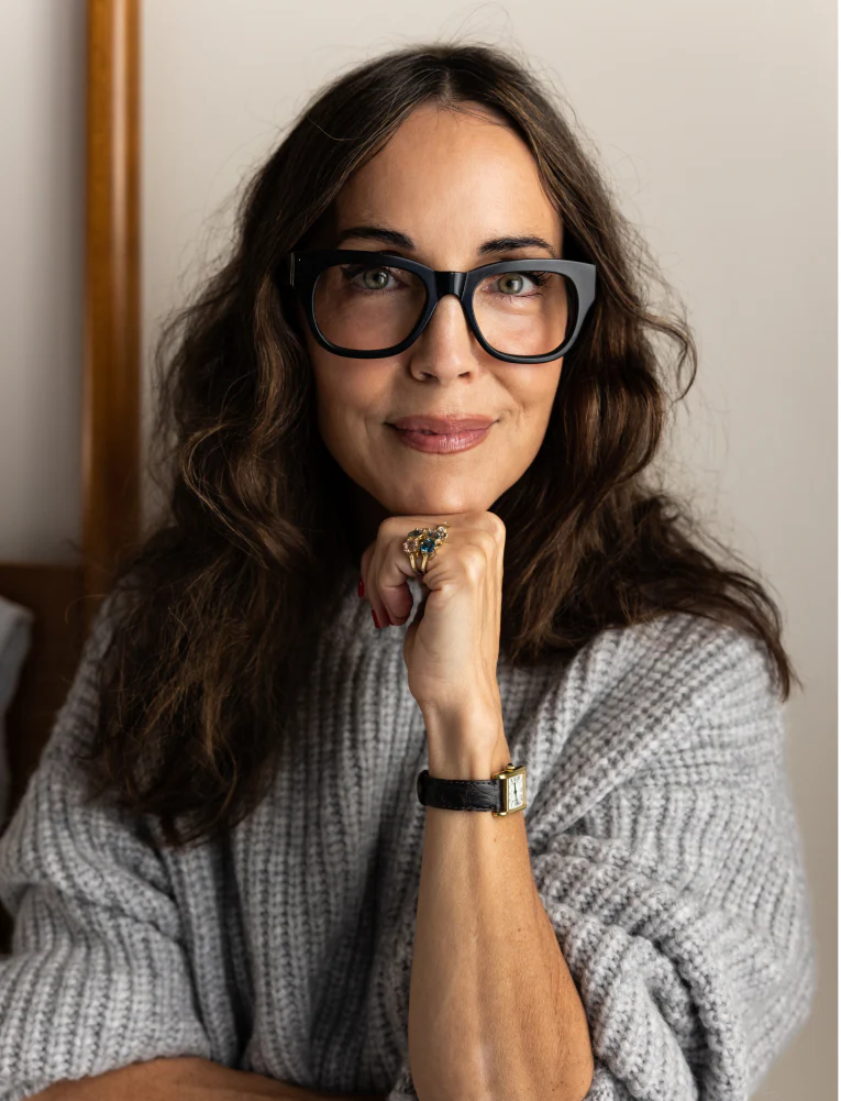 Larissa Mills wearing a gray sweater, a stack of gold gemstone rings, a black watch, and black glasses