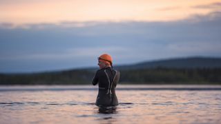 A woman in wetsuit going into a lake for some wild swimming at sunset