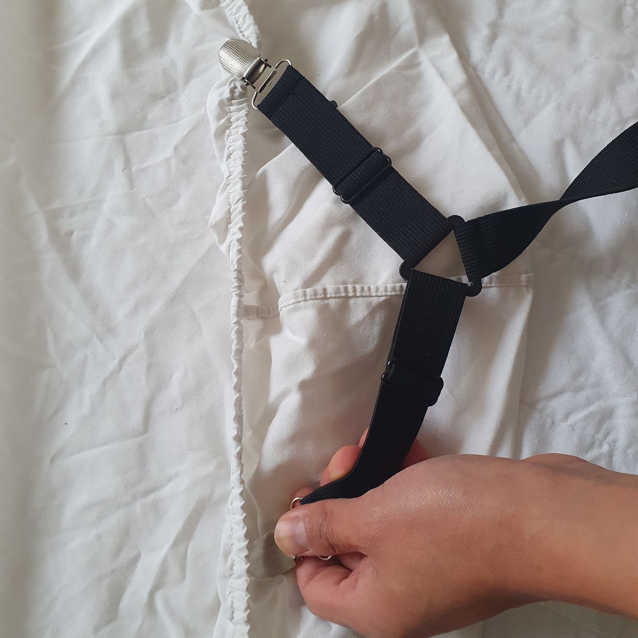 Black elasticated sheet straps being fitted to a white fitted sheet