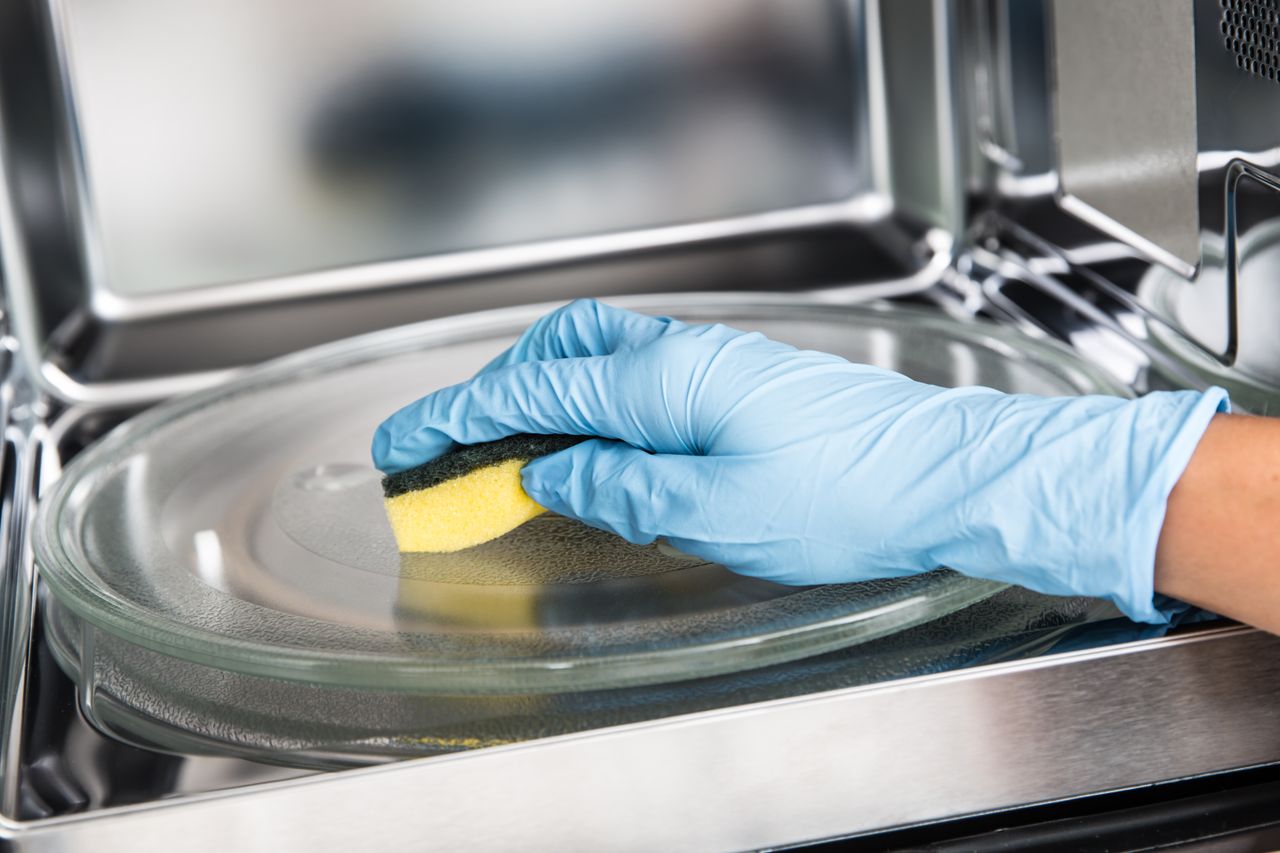 A person cleaning the inside of a microwave.