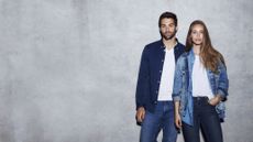 A man and a woman rocking double denim, standing against a concrete wall