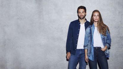 A man and a woman rocking double denim, standing against a concrete wall