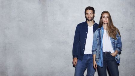 A man and a woman rocking double denim, standing against a concrete wall