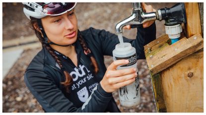 A female cyclist fills their drinks bottle with water at an outdoor tap