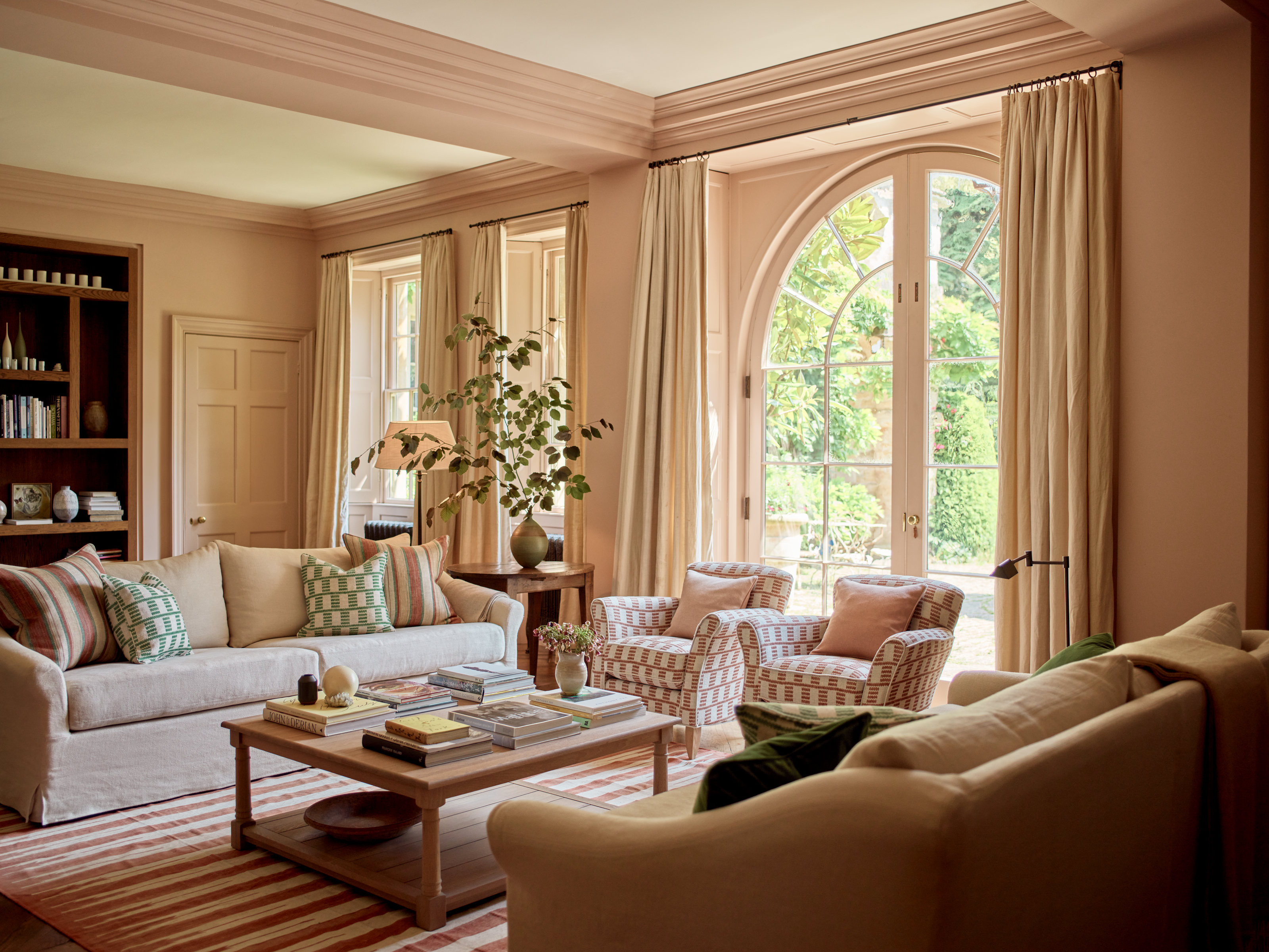 A living room with pale pink walls and woodwork, patterned upholstery, and a striped rug