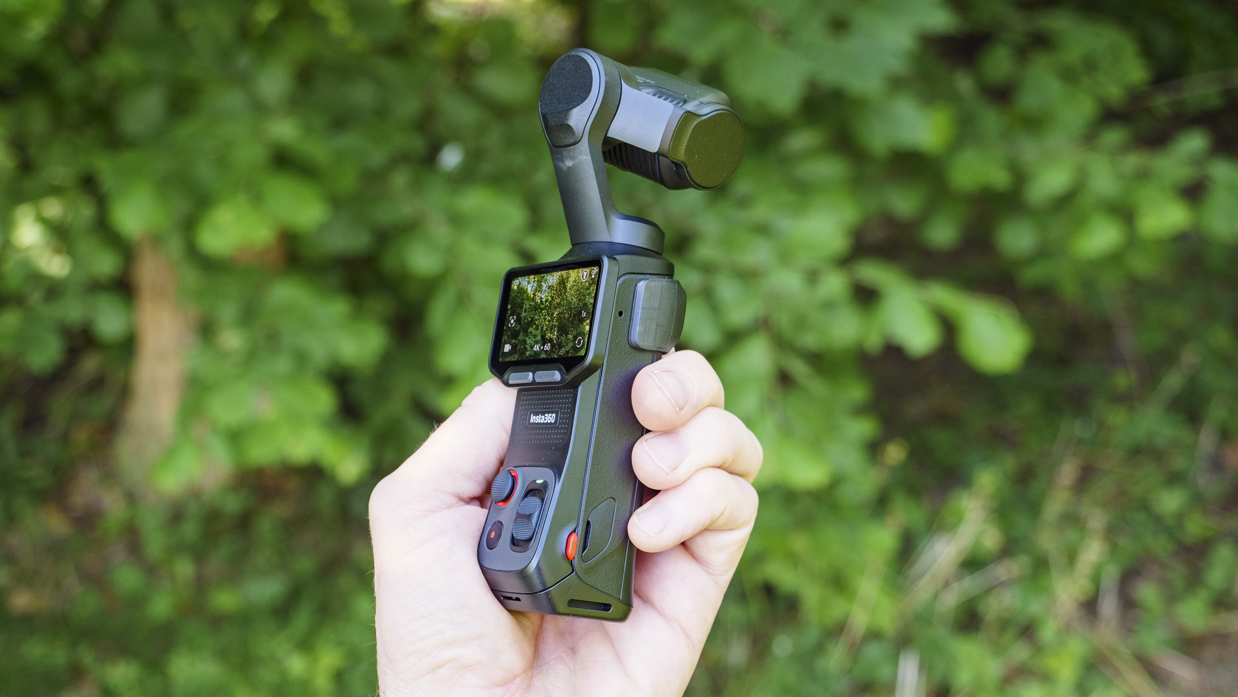 Insta360 Luna Ultra vlogging camera in person's hand, screen rotated and 4K 60p video active, leafy background