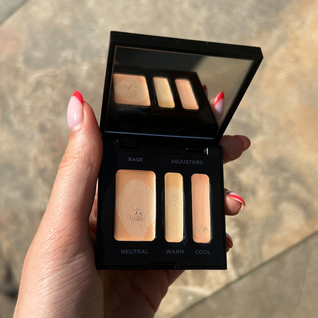 Hand holding an open Laura Mercier Secret Camouflage Complexion Perfector