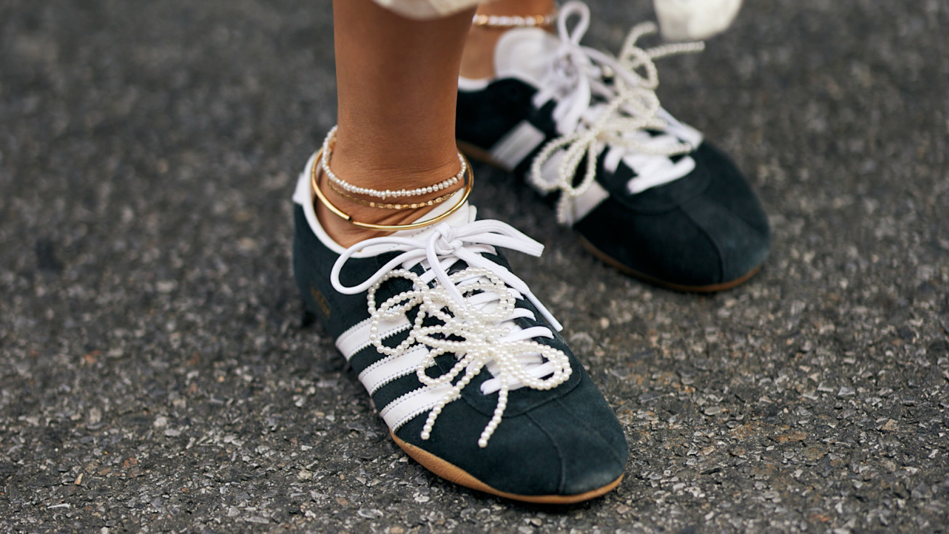 woman wearing black and white adidas sneakers with pearl laces and anklets 
