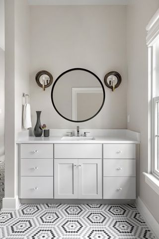 bathroom with grey patterned floor tiles, grey vases, mirror, wall lights, white vanity, cream walls
