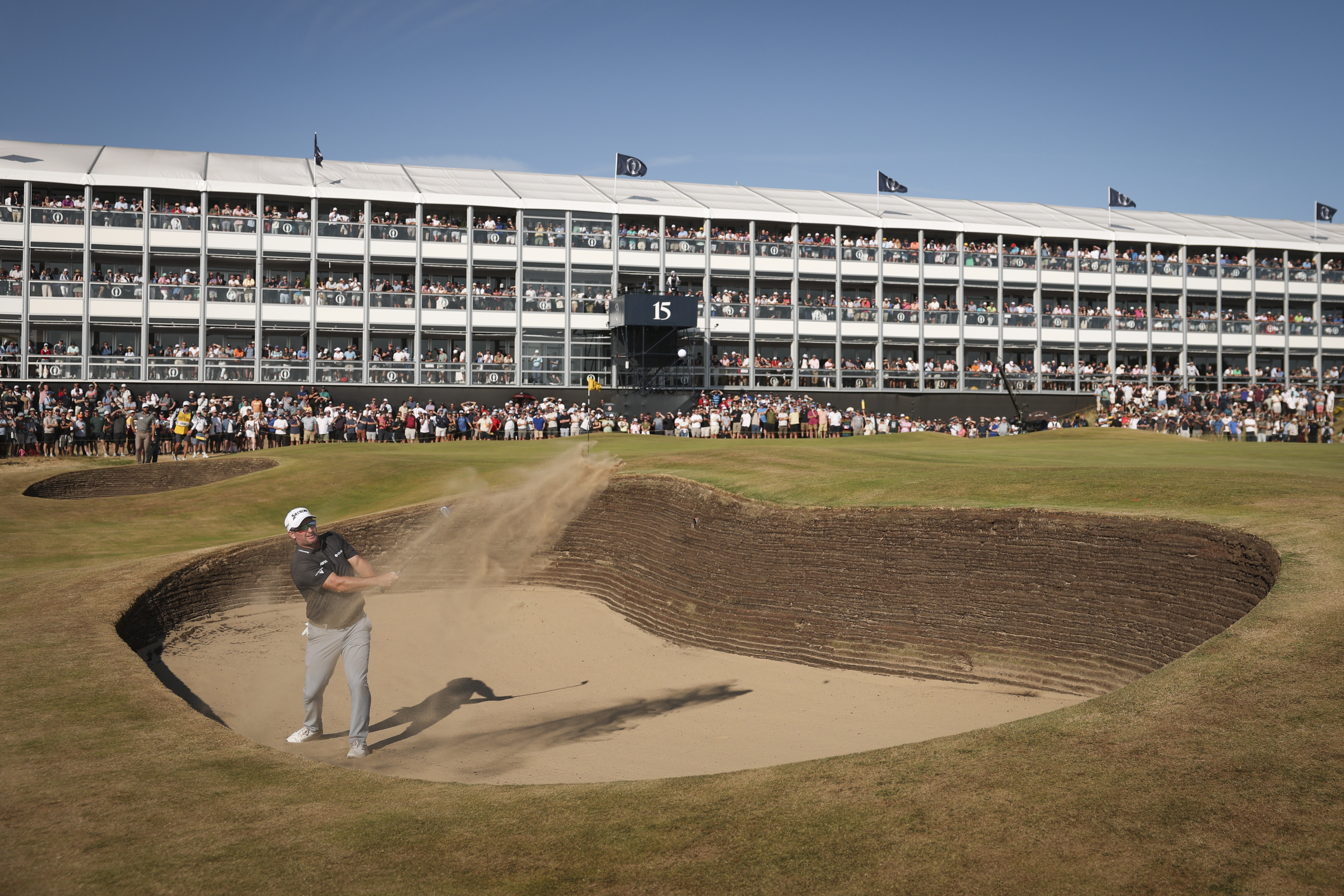 2026 Open champion Ryan Fox plays out of a bunker at Royal Birkdale's 15th hole with a huge grandstand in the background
