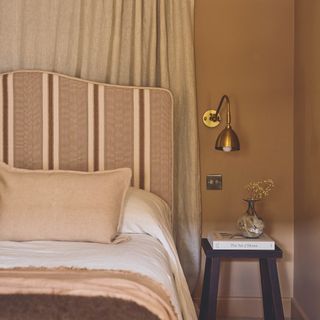 bedroom with headboard in striped upholstery with wall curtain behind bed and brass wall light