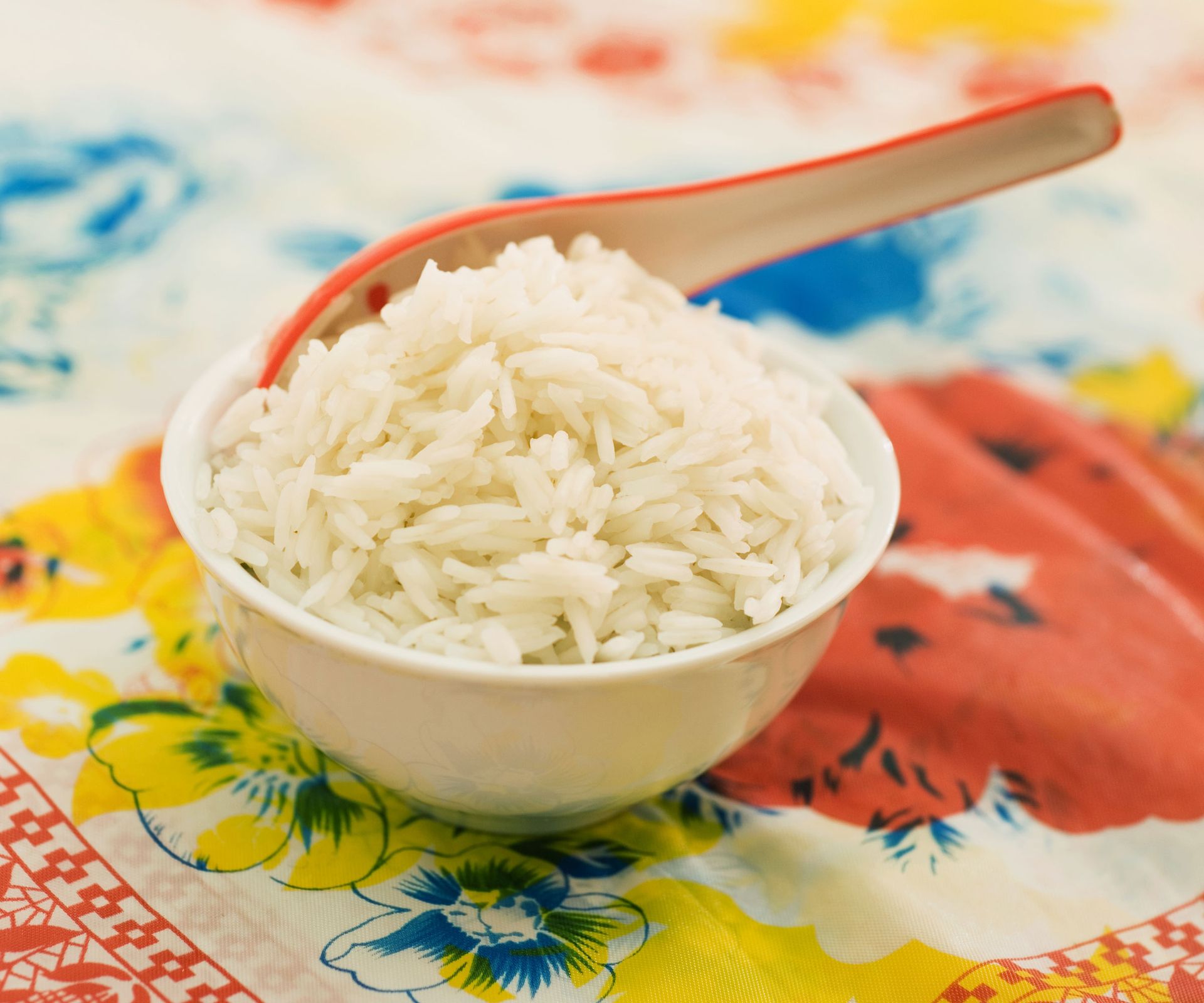plain cooked rice in a bowl with an orange spoon on colorful table linen
