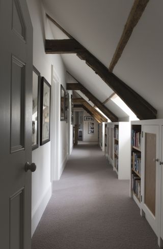 Corridor landing with neutral decor and sloping beamed ceiling and built-in bookshelves