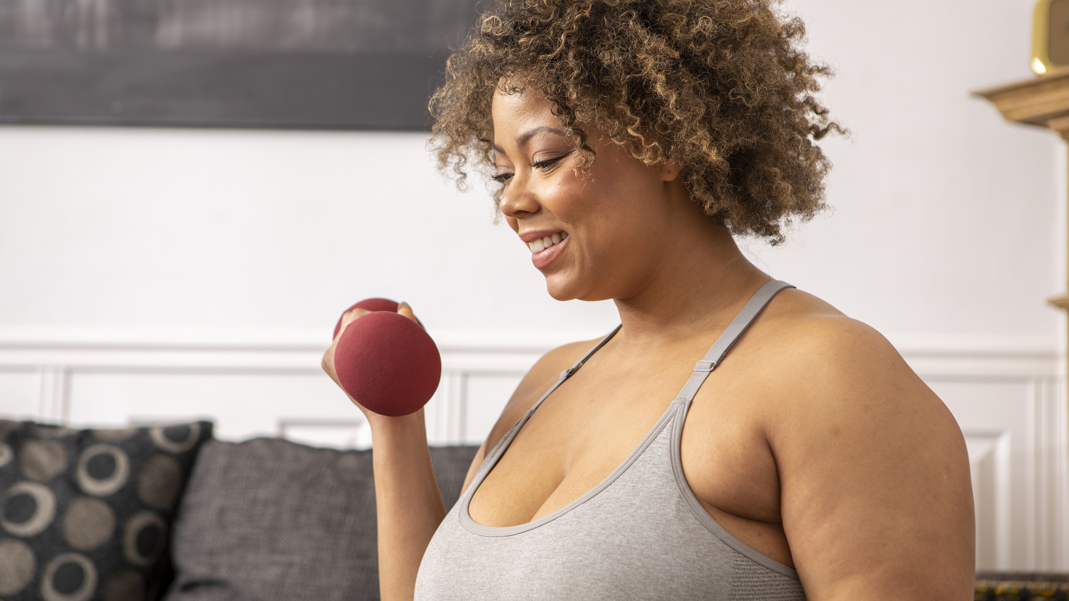 Woman holding a dumbbell by her shoulder in a domestic setting