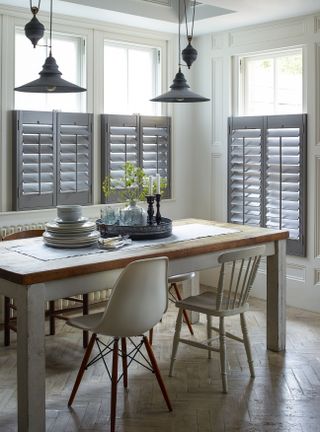 rustic dining room with half shutters on the windows, pine top table, mix of modern and old style chairs