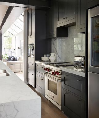 A black galley kitchen with chrome appliances leading into a white living room