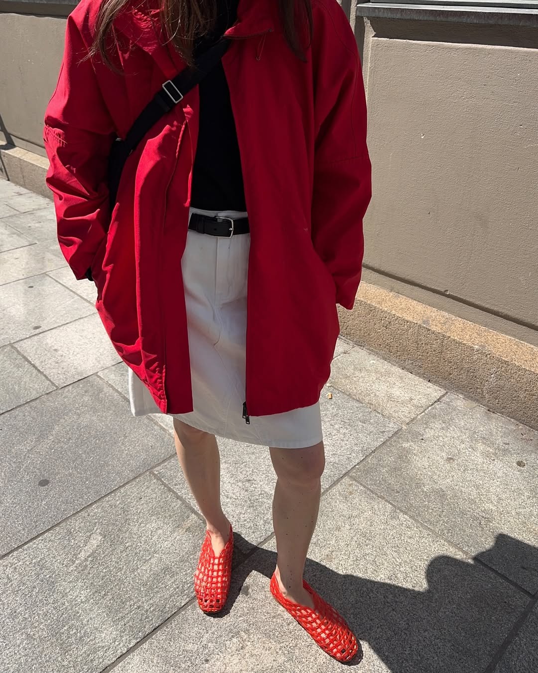 a woman wearing red jelly flats, a white skirt, black buckle belt, and red zip up jacket