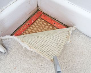 pulling back the corner of an old cream carpet to reveal underlay - Carpet removal
