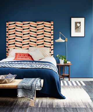 An example of bedroom wall light ideas showing a bold patterned headboard, a blue bed and a white wall light with a visible cable