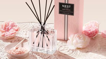 One of the best reed diffusers in our buying guide: The Nest New York Himalayan Salt & Rosewater Reed Diffuser unboxed with packaging and fresh roses in background