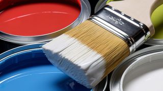 Close-up of paintbrush with white paint on it on top of open tins of red, blue, green and white paint
