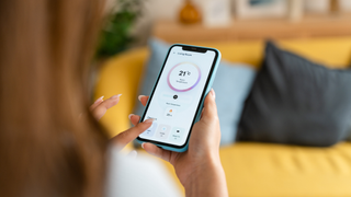 Back of person who is setting their home temperature on a smartphone with a yellow sofa blurred in the background