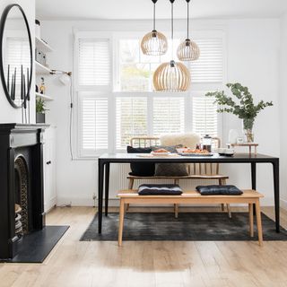 White dining room with a black dining table, hanging lights and a black fire place