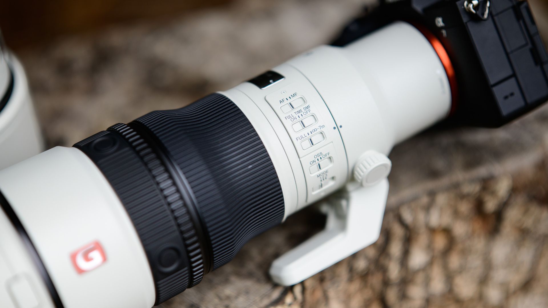 Sony FE 600mm F6.3 GM OSS super-telephoto lenses on a tree stump, attached to a Sony A7R V camera, closeup of the lens controls
