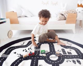 boy child playing on the Harmony at Home Boutique Storage Bag And Play Mat in a white room with a white bed