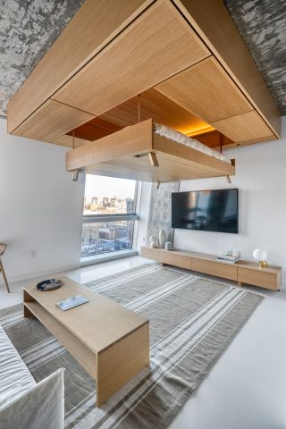 An apartment at The Smile in New York with modular moving furniture by Bumblebee Spaces. The picture shows the wooden bed being raised above the room and into the ceiling.