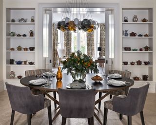 Dining room with grey chairs, wooden table, white walls and shelving