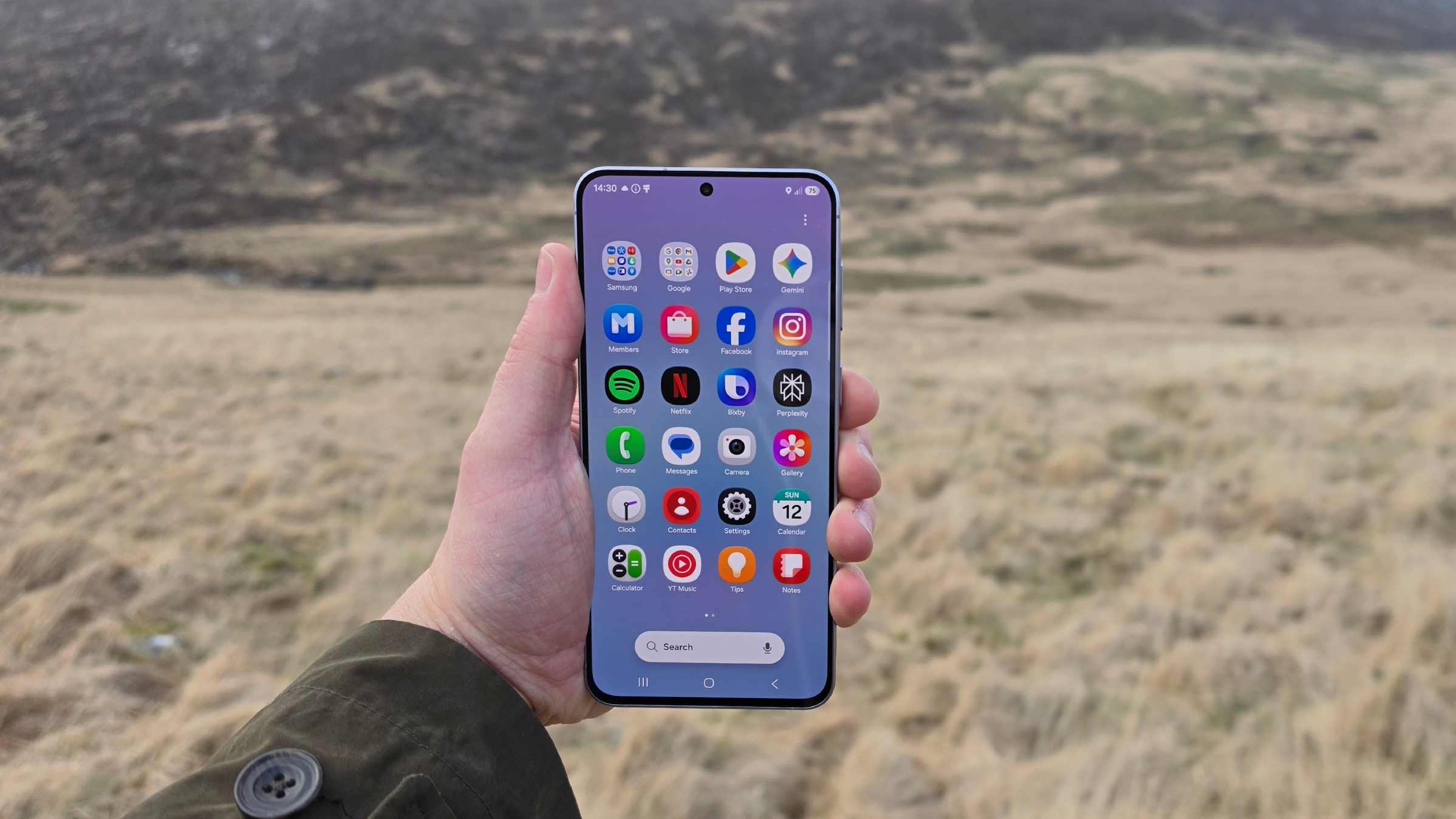 The Samsung Galaxy A57 being held over a field, showing its app gallery.