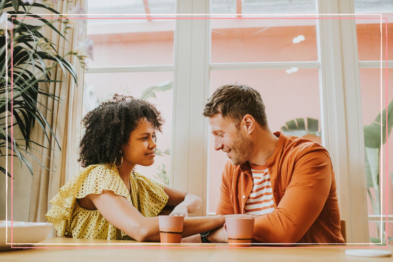 A heterosexual couple looking at each other while sat at a table drinking coffee