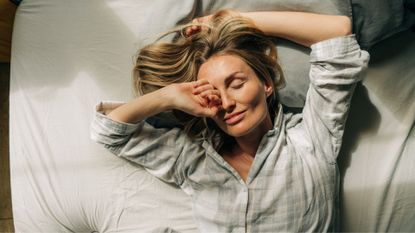 Woman with arms raised above head, smiling as she wakes up in the morning in pyjamas under bedsheets after learning how to stop snoring