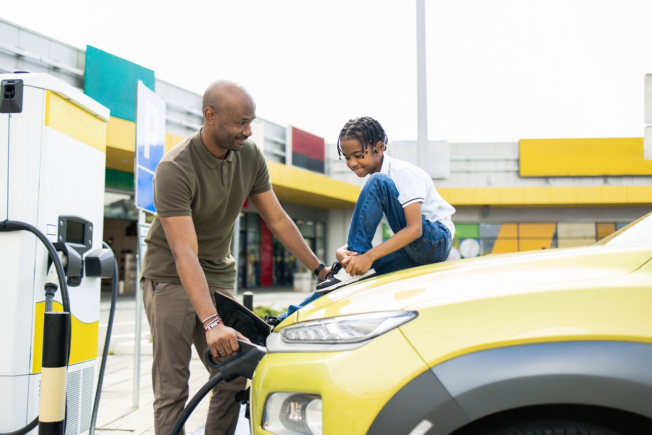 Happy father and son are at the charging station for their electric car