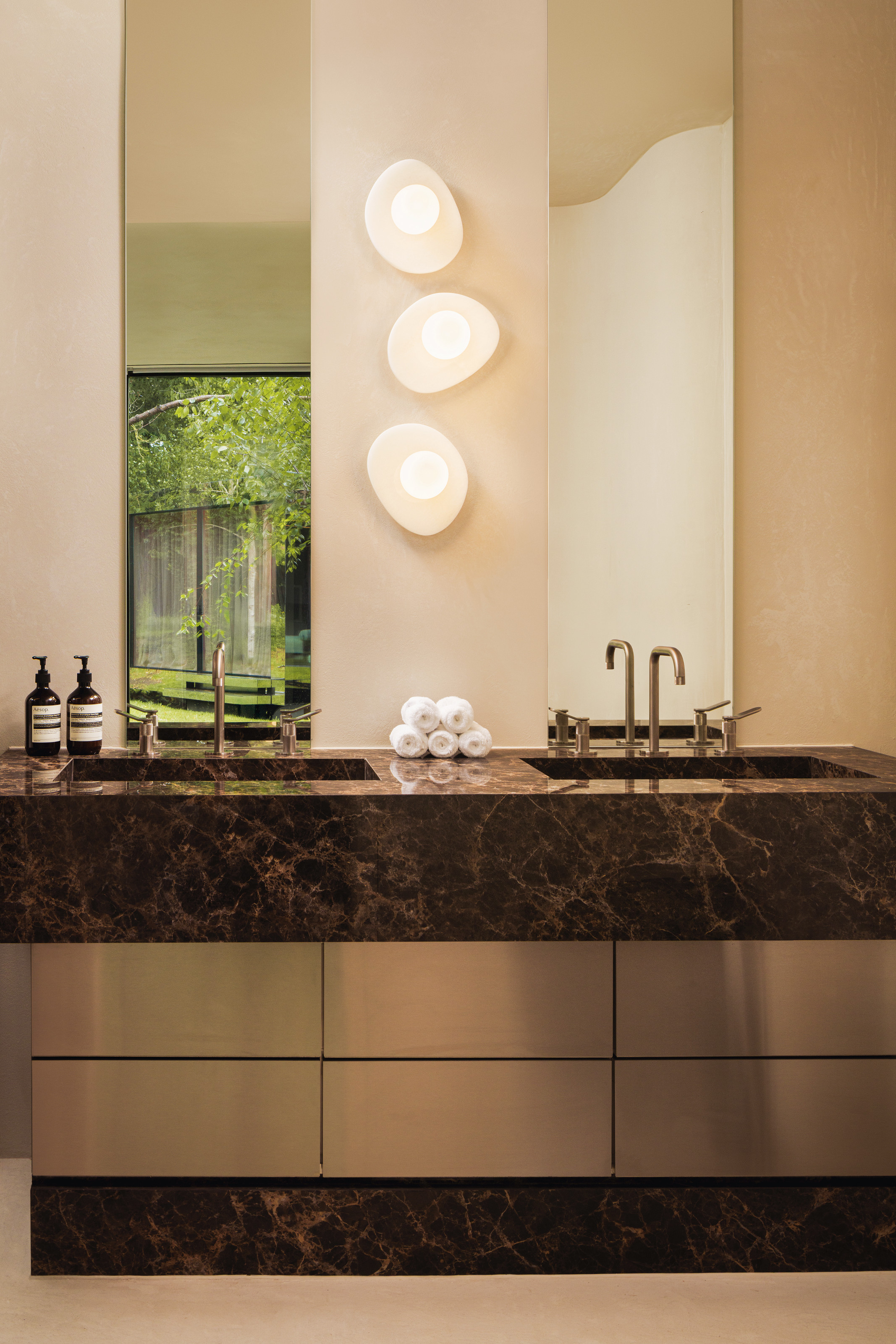 Bathroom vanity in brown marble and stainless steel with twin sinks and organic-shaped wall lights