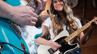 A person playing a turquoise Strat on the left and a woman playing a Telecaster on the right while smiling