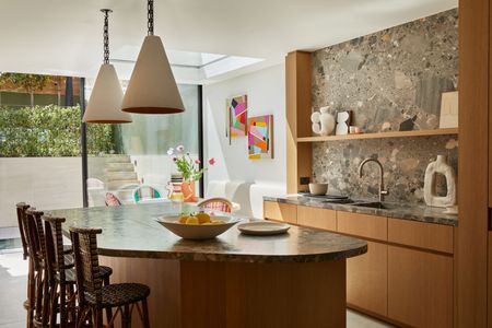 a luxury kitchen extension with brown natural stone surfaces. a skylight sits above a dining area with colorful artwork and vases