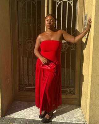 Woman wearing a strapless red maxi dress and mesh ballet flats.